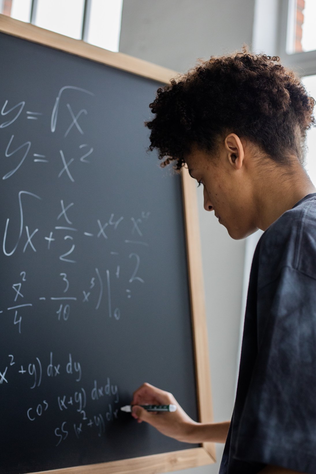 Serious black student solving math equation on blackboard